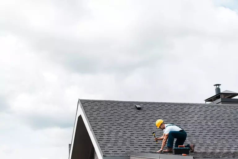 A contractor on the roof of a home performing roof maintenance to damaged shingles.