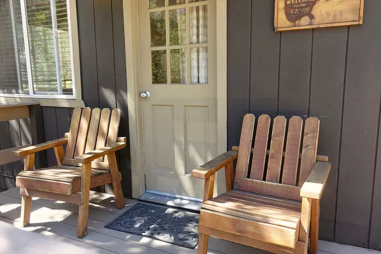 A new, sturdy beige entry door to a dark brown log cabin that has a small front porch with a wooden outdoor seating set.