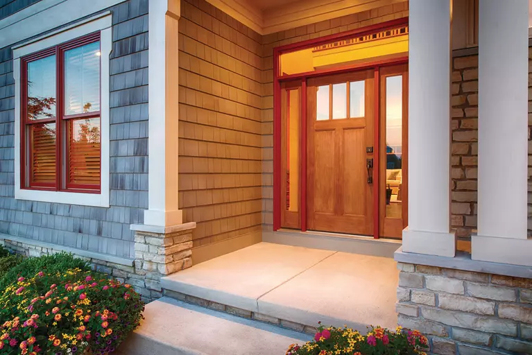 The entryway of a multi-level home with a large wooden entry door and windows on the side.