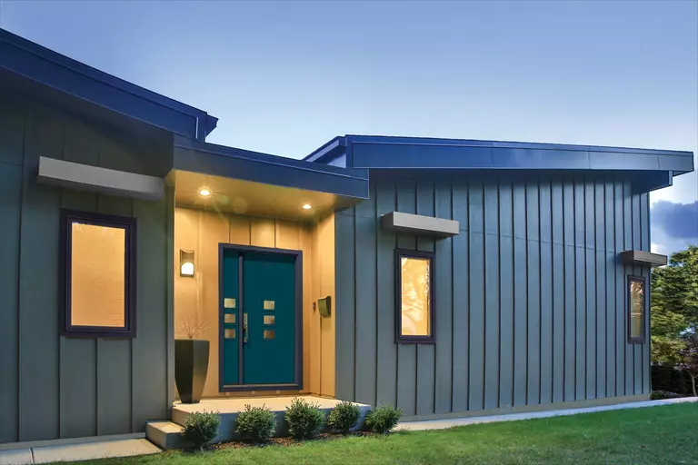 A modern home’s exterior pictured at dusk. The door is marked with six small windows arranged vertically.