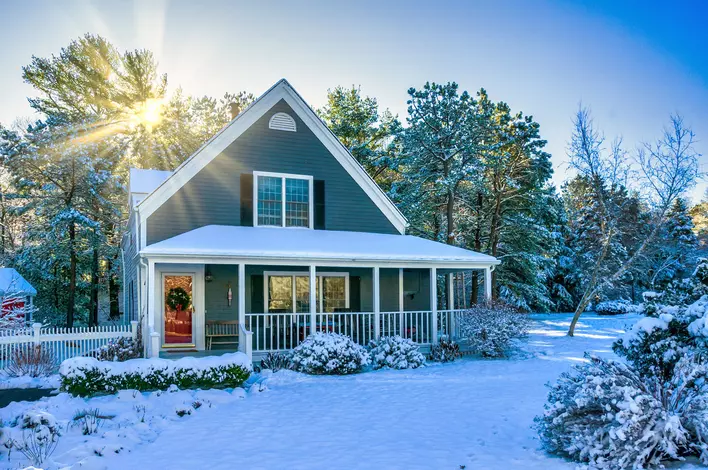 A beautiful home surrounded by trees and shrubbery covered in snow.