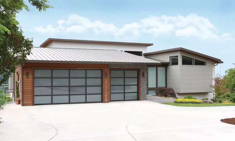 A modern house with two full-view glass garage doors of different sizes.