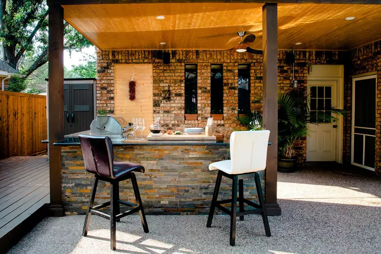 An outdoor kitchen built in the back patio of a home, with a guest bar and an open space for hosting guests.