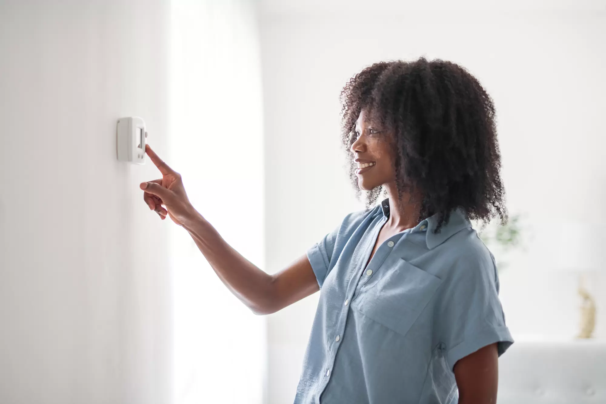 Woman adjusting a wall-mounted thermostat.
