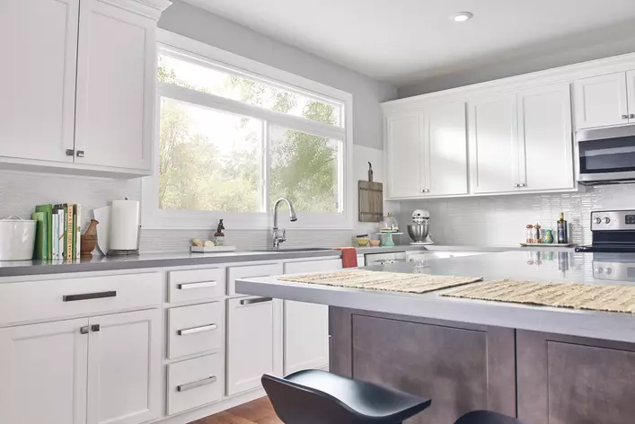 A kitchen with white cabinets and a large island with a large window above the sink