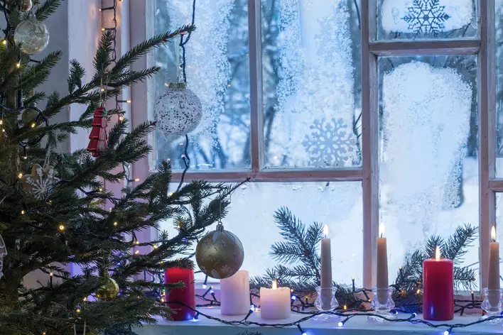 Candles, Christmas lights, and a Christmas tree with colorful ornaments surrounding a
window of a home with snowflake decals on the glass panes.