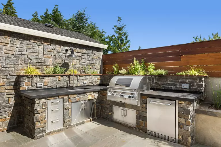 An outdoor grilling setup, complete with storage for plates and cutlery and a sink for doing dishes outdoors.