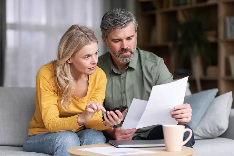 A man and woman looking at papers while sitting on a couch.