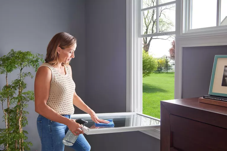 A woman cleaning a window with a tilt-in sash in a home.