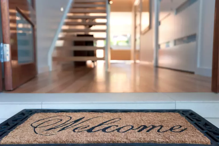 A welcome mat in front of an open entry door.