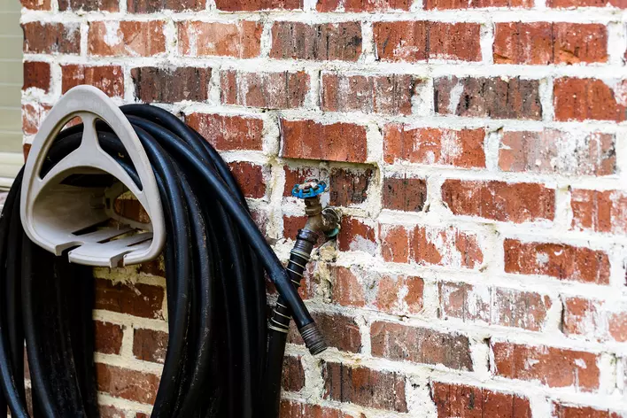 Rubber garden hose hanging next to the brick wall of a home