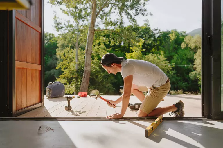 Man using a hammer and level to prepare the sill of an entryway of a house