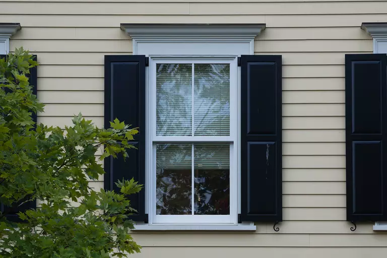A window of a home with black functional exterior shutters.