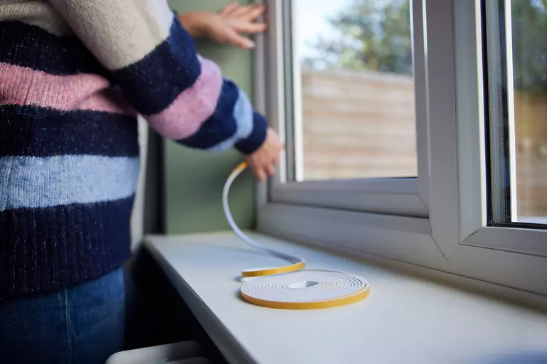 A coil of weatherstripping sitting on a window ledge and being applied by a homeowner.