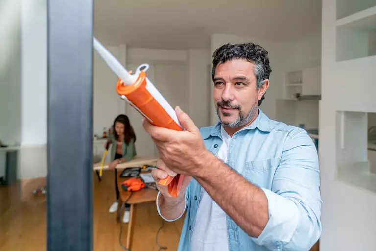 A man using a caulking gun on the edges of a door frame.