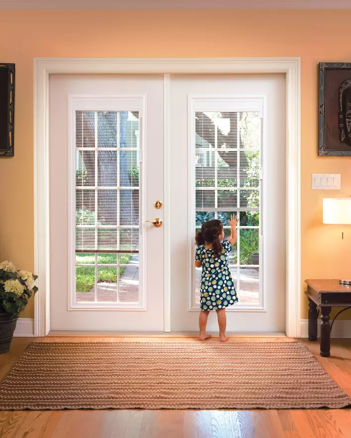 A child standing in front of a patio door with blinds