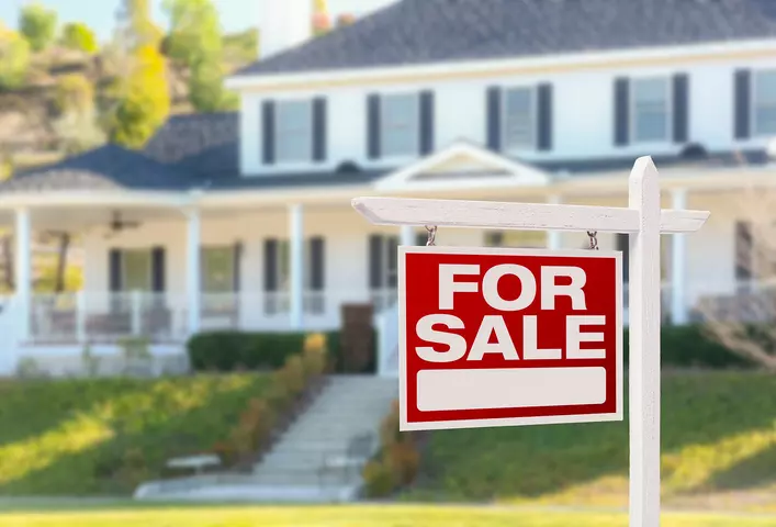 A for sale sign in front of a large white home with black exterior accents.
