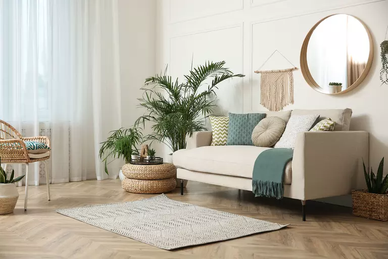 A living room with neutral color furniture, plants, and a natural fiber rug for decor.