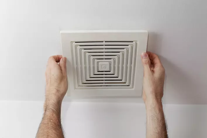 A man placing a fan in the ceiling of a room to circulate air and eliminate moisture
buildup.