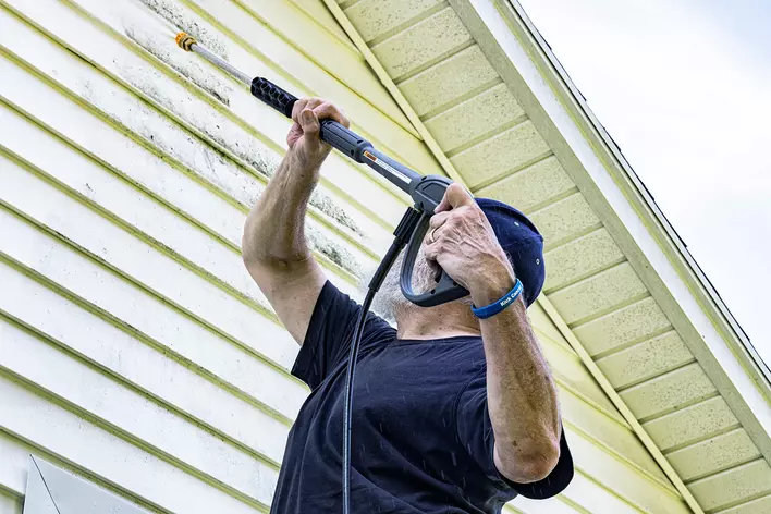 A man power washing the exterior of his siding home to increase curb appeal.