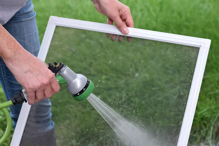 A person uses a garden hose attachment to spray a removable window insert.