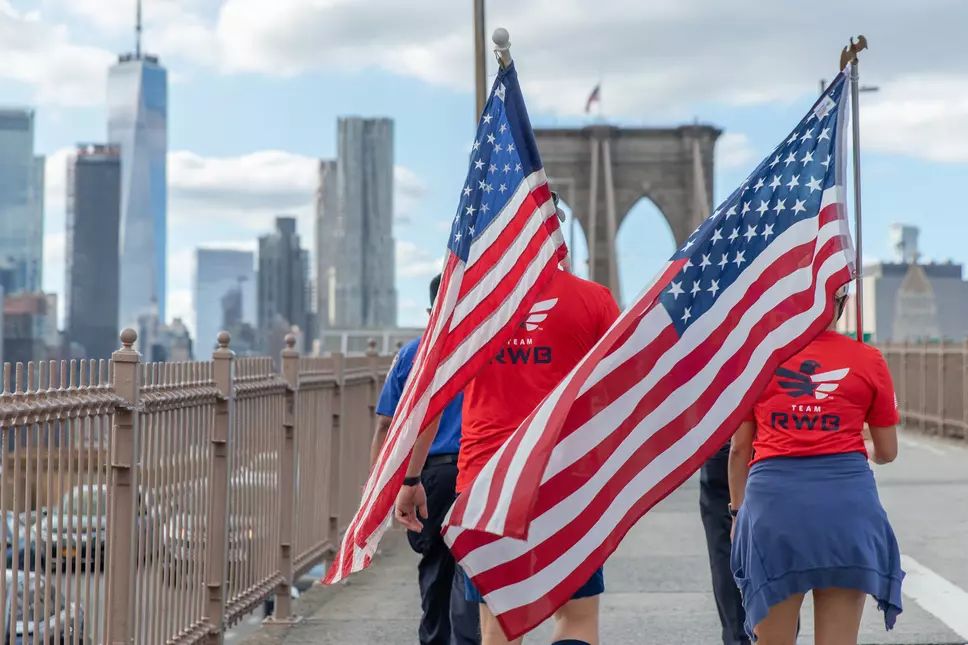 Supporters of Team Red, White, and Blue carry American Flags across a New York City bridge