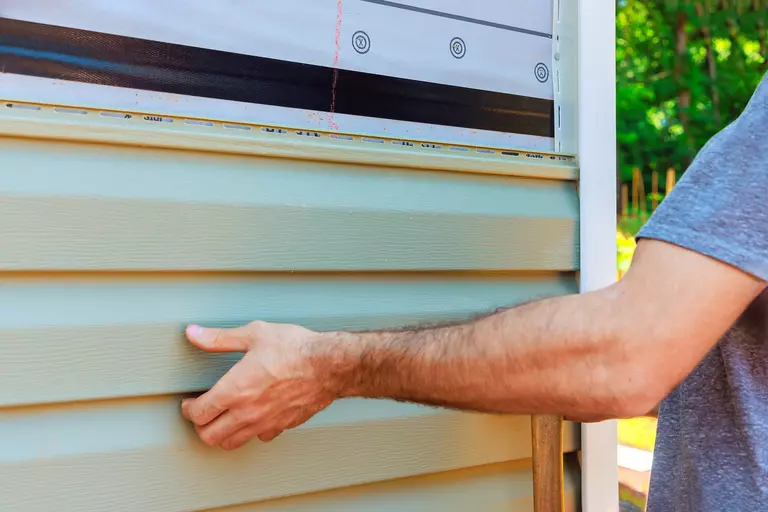Man installing a piece of vinyl siding on top of others on the side of a home.