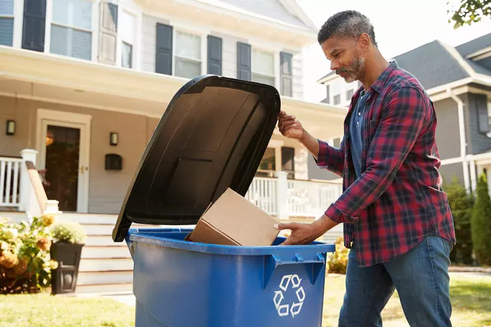 A man recycling a cardboard box to reduce his carbon footprint.
