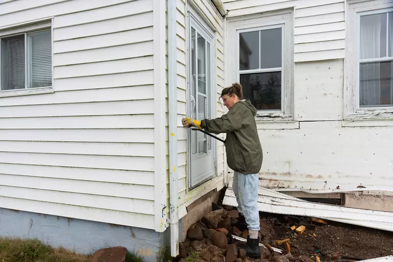 Woman removing old siding with a crowbar.
