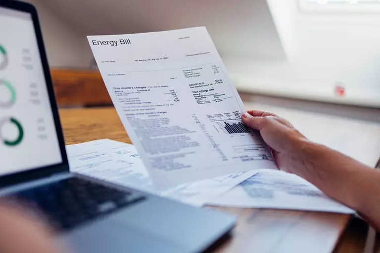 Person holding an energy bill next to a laptop.