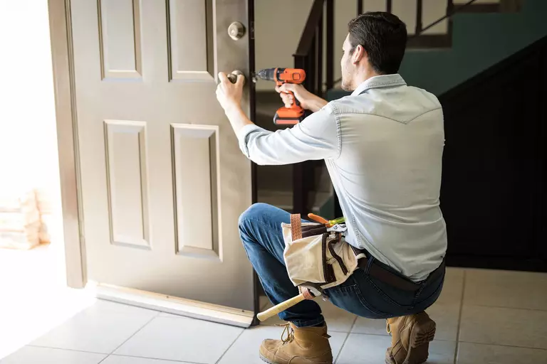 Worker performing an exterior door installation on a home while using a drill.