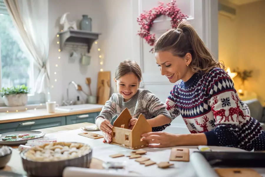 A granddaughter and her grandmother decorating a gingerbread house