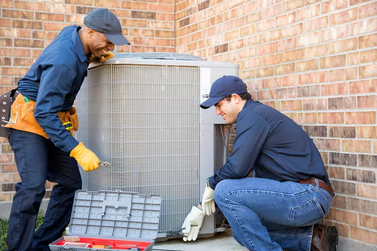 Two men performing an HVAC inspection on the side of a brick home.