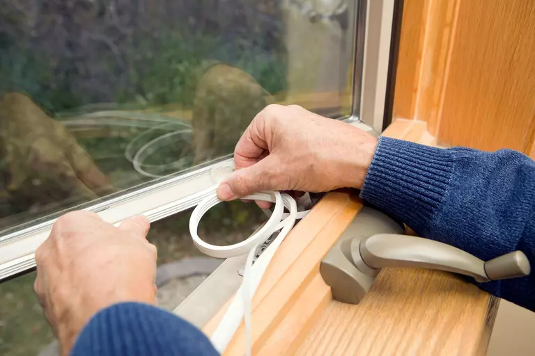 Person applying weatherstripping to the edges of a window frame.