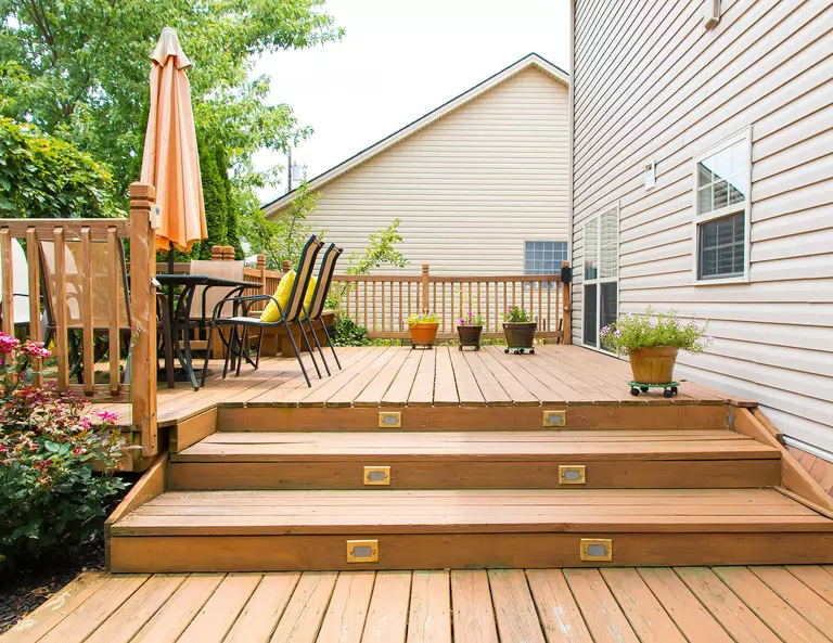 A multi-level back deck extending off a siding home that is decorated with an outdoor dining set, an umbrella, and plants.