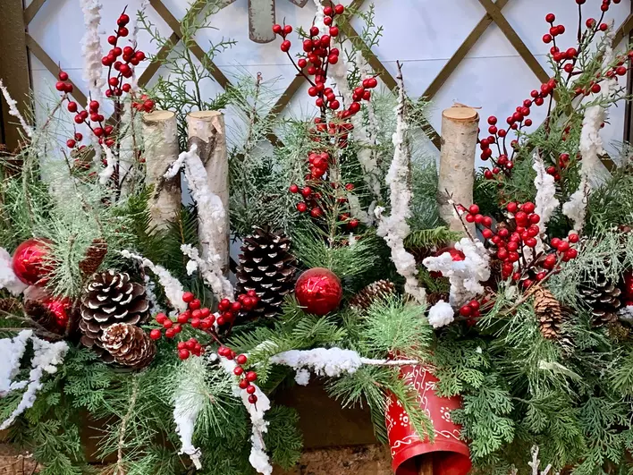 A holiday bundle filled with pine branches, berries, and Christmas ornaments in a
window box.