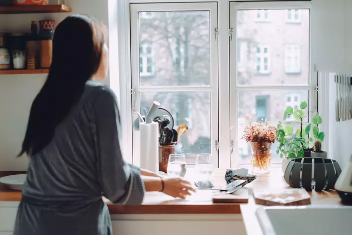 Woman preparing breakfast for her family in the kitchen at home in front of a laminated
        glass window.