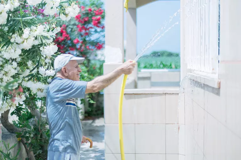 A man using a hose to spray the exterior windows of a home.