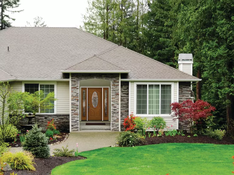 A home’s lawn and front porch with a brown door and a pair of sidelites.