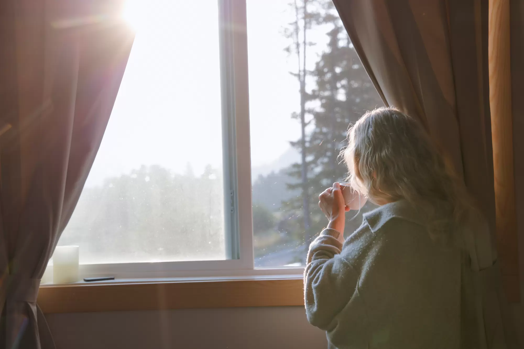 Woman enjoying a warm drink beside a sunlit window.
