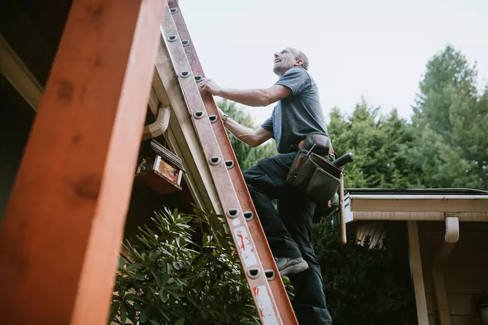 Man climbing a ladder as he checks his roof and gutters.