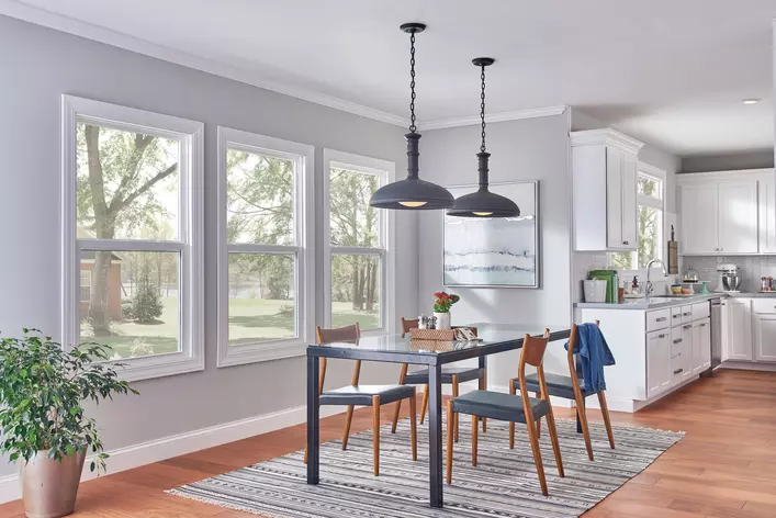 A dining room with a table and chairs around it in front of three dining room windows