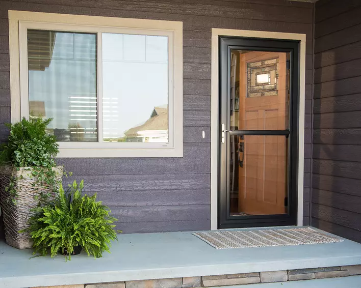 A black storm door on the entryway of a dark-colored home.