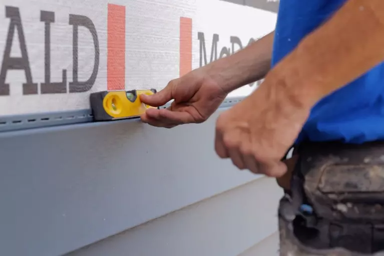 Close-up of a Window World employee using a level tool to check the siding width is even.