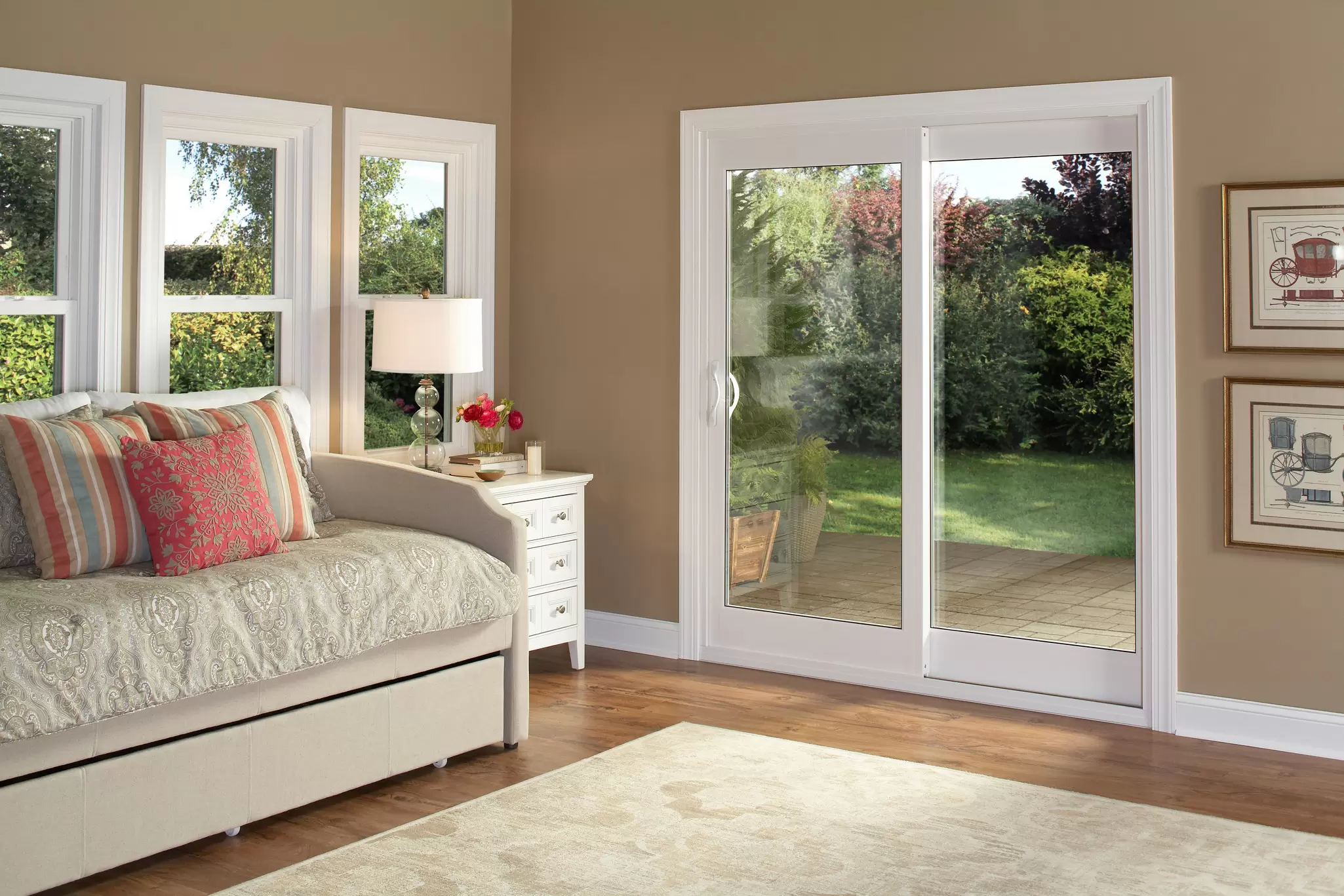 White sliding patio door beside double-hung windows in a living room overlooking a green backyard.