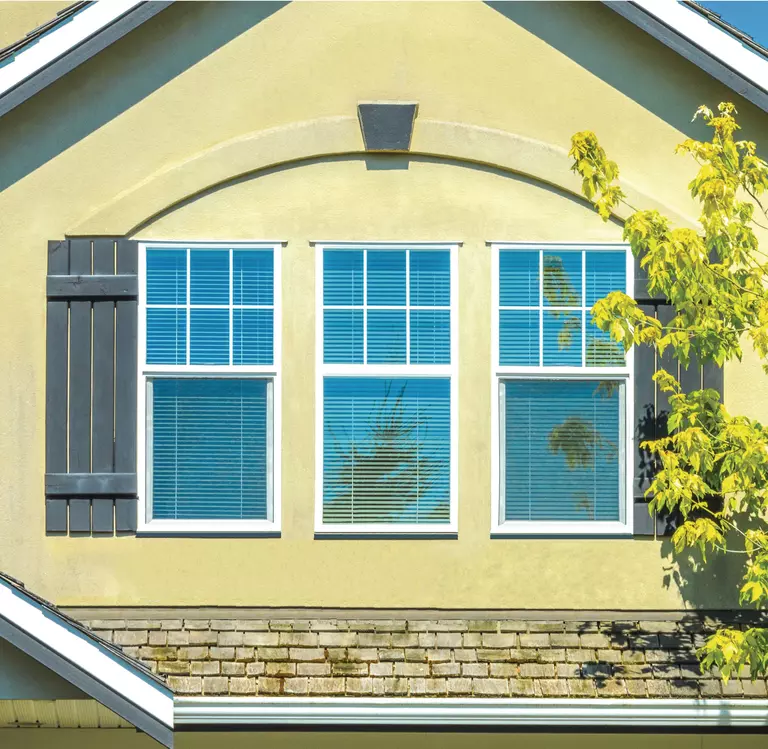 Yellow house with three windows in a row; the outsides have gray exterior window shutters.