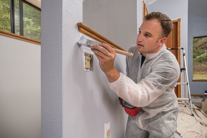A man cutting in the edges of a gray DIY home renovation paint job.