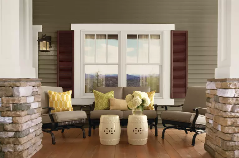 The deck of a home with patio seating with a large double-hung window using brown louvered shutters.