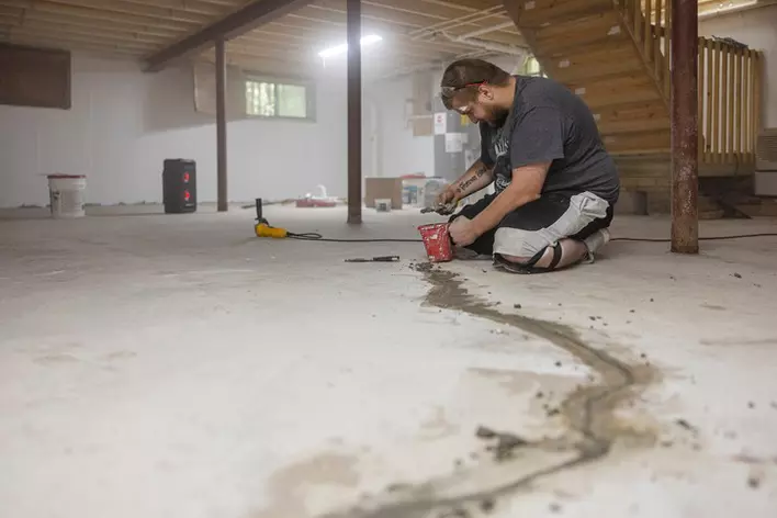 A person sitting on the basement floor of a home trying to fix the home’s foundation