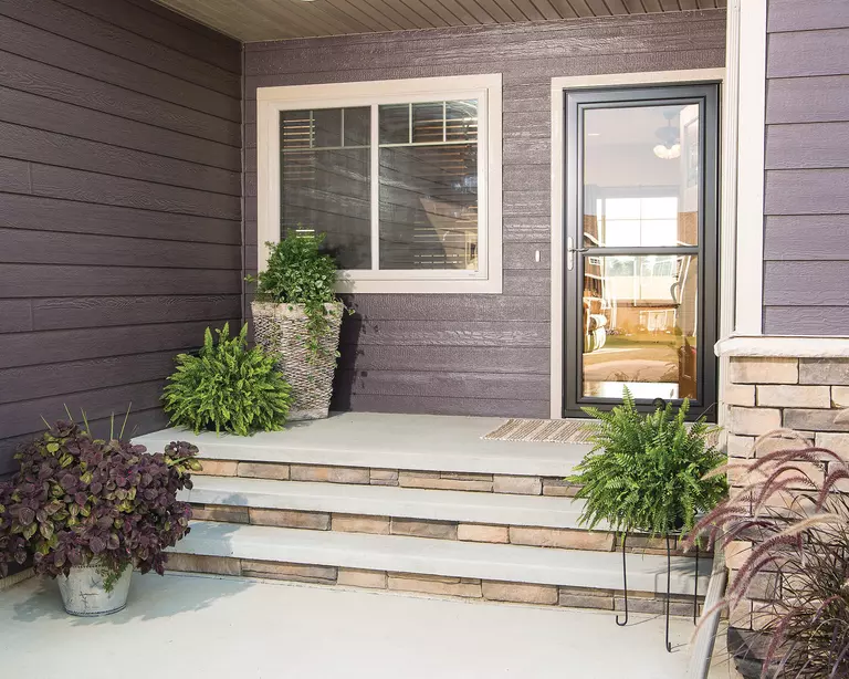 A home with gray vinyl siding and a full-view storm door allowing a view of the front yard.